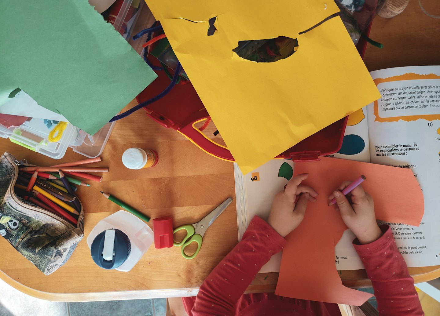 Kinderhände malen auf orangefarbenem Papier mit Bastelmaterial.