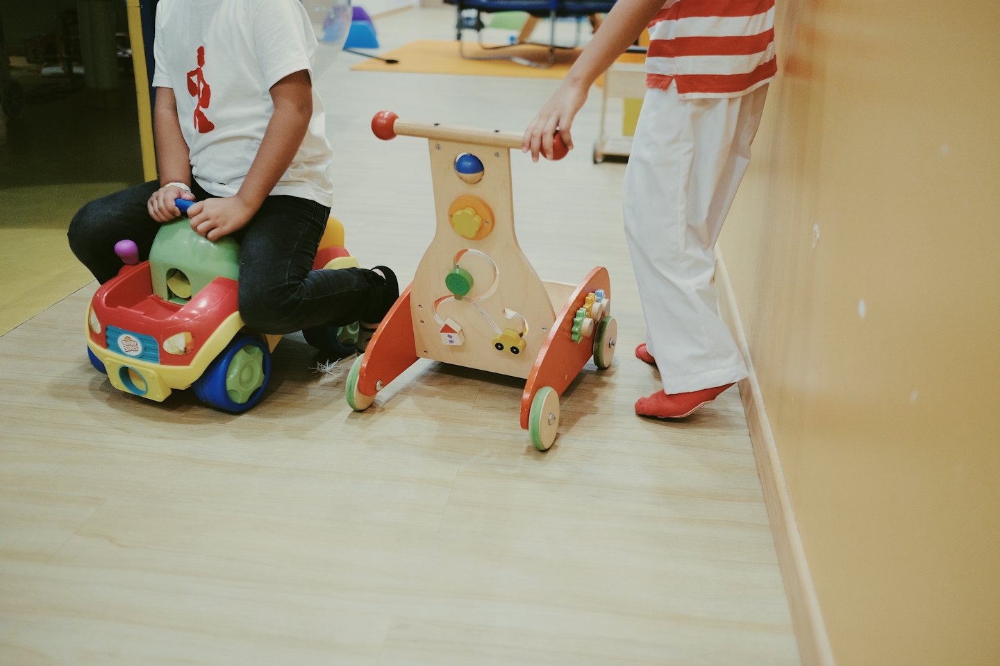 Zwei Kinder spielen mit Spielzeug auf einem hellen Holzboden.